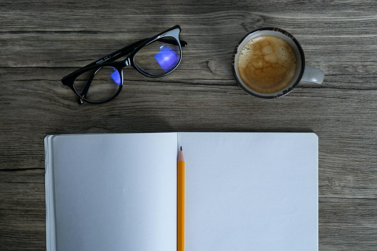 An open notebook with a pencil and coffee on a table