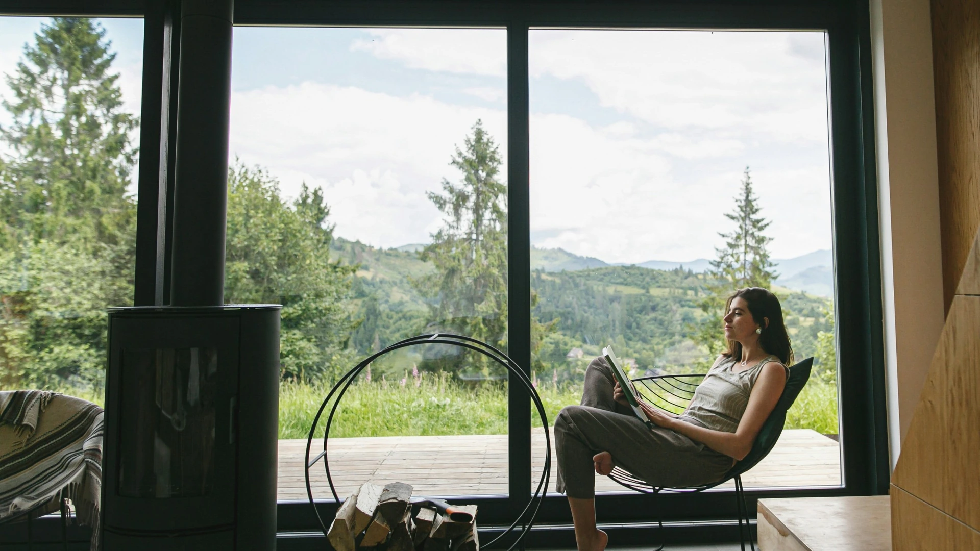 A woman reading at home beside a window overlooking the countryside
