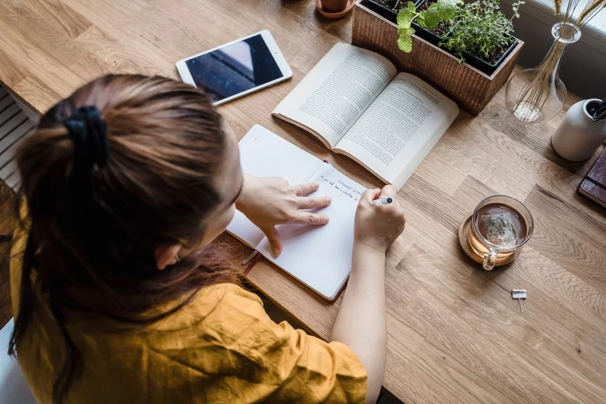 A woman writing at a table with a notebook and papers