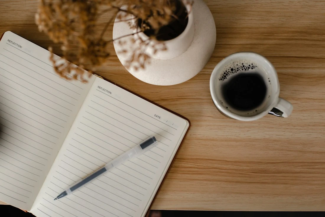 A notebook and coffee on a wooden desk in daylight